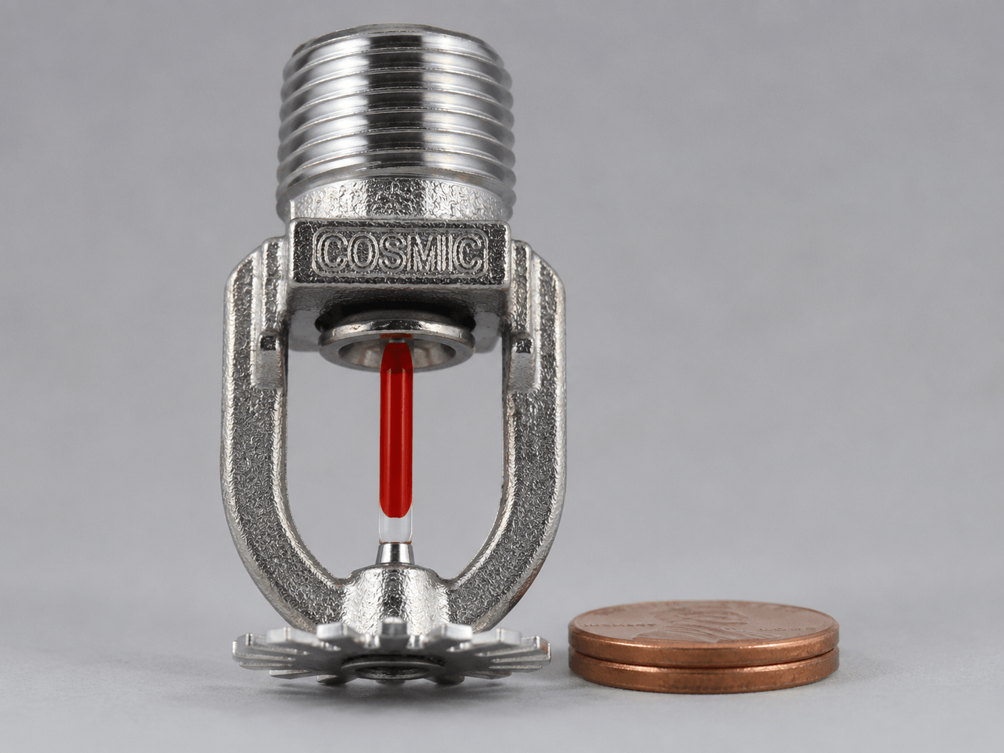 A fast-response (quick-response) pendant sprinkler head with a 3mm red glass bulb shown beside a U.S. penny for scale — two stacked pennies run roughly 3.0–3.1mm thick, just slightly more than the bulb's 3mm diameter